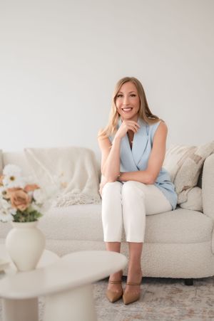 Someone sits comfortably on a light gray couch in a bright living room with a vase of flowers nearby.
