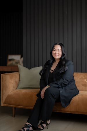 Professional office portrait with someone seated comfortably on a brown leather couch against a dark gray wall.