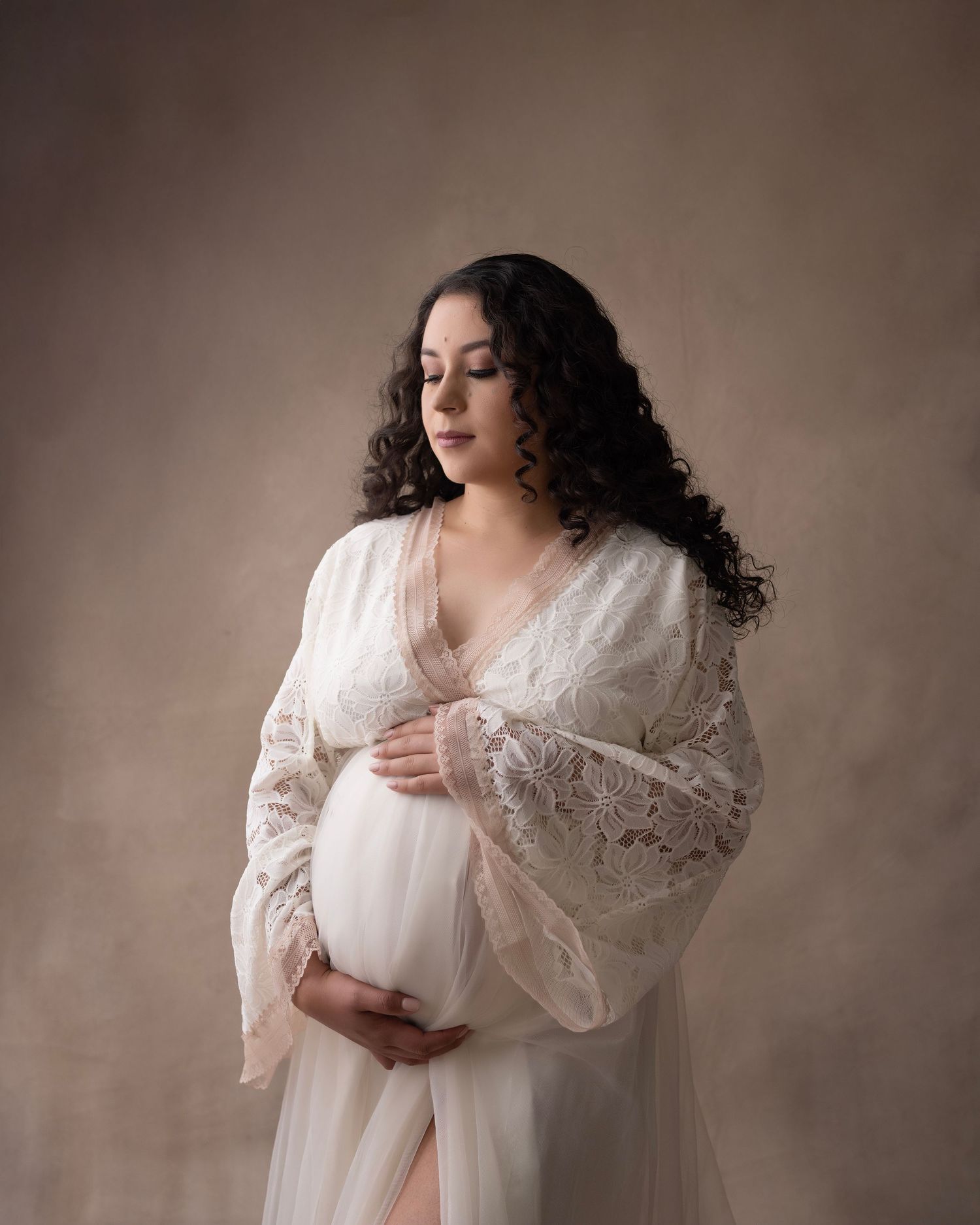 Intimate maternity photograph featuring delicate white lace dress and natural curls.