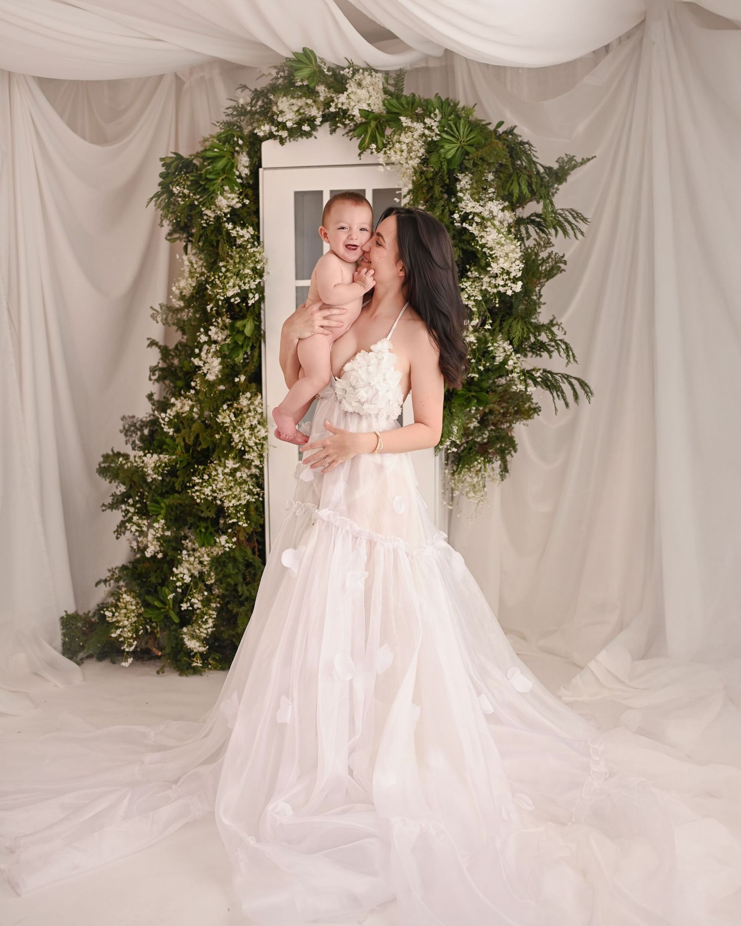 White draped photography studio with elegant floral arrangements framing a vintage French door.
