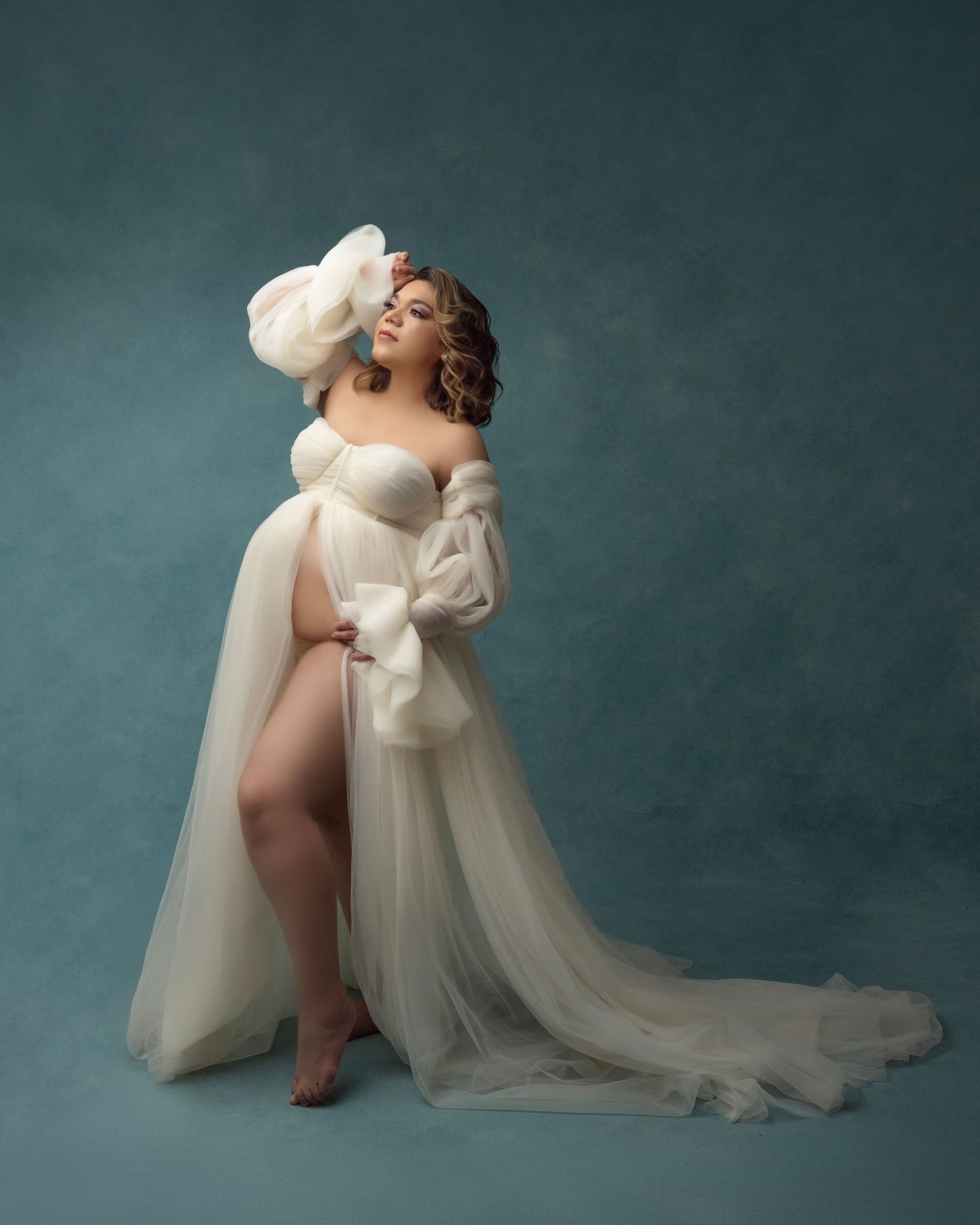 Artistic maternity portrait in off-shoulder cream gown with dramatic train.