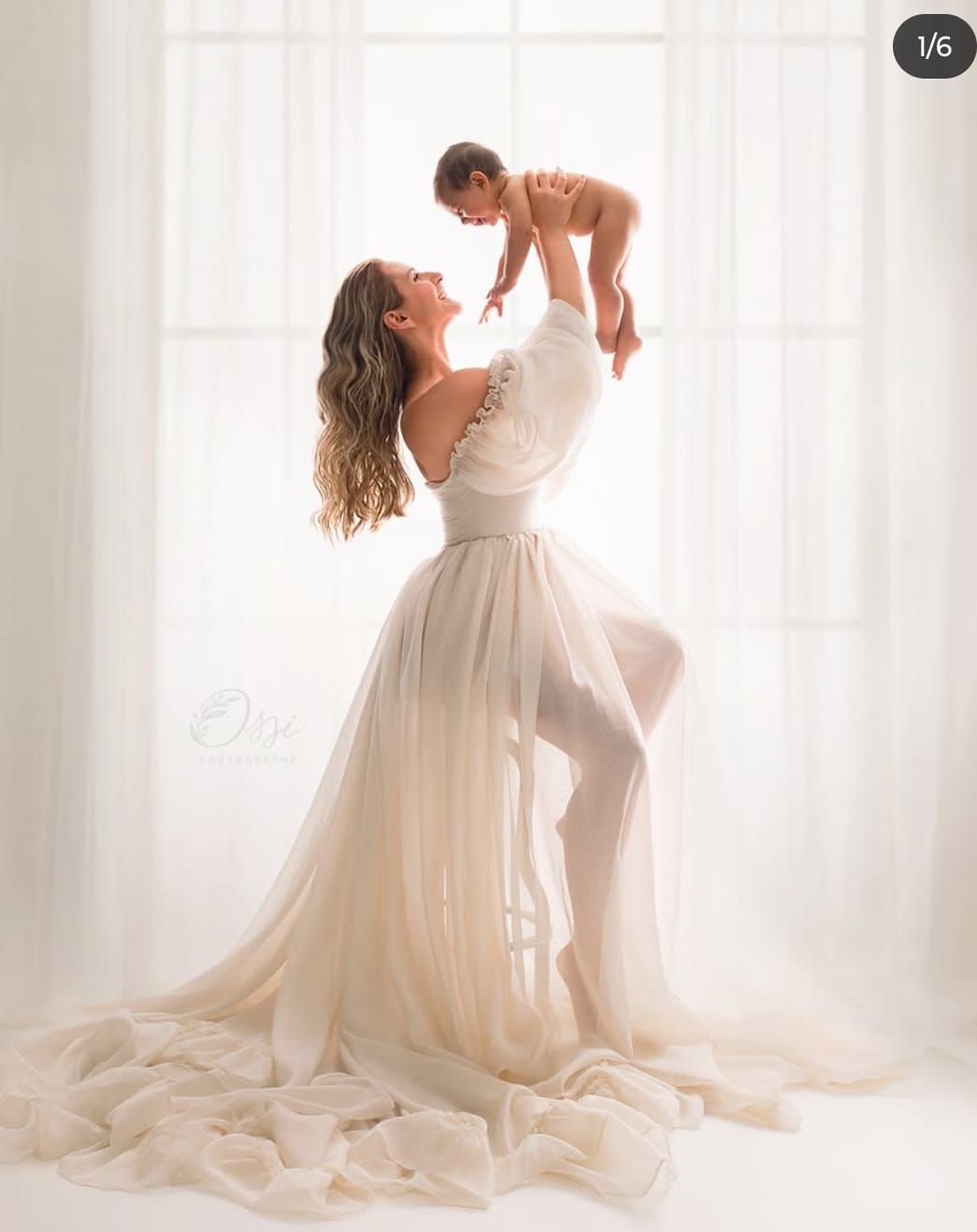 Mother and baby portrait in flowing white dress against bright window.