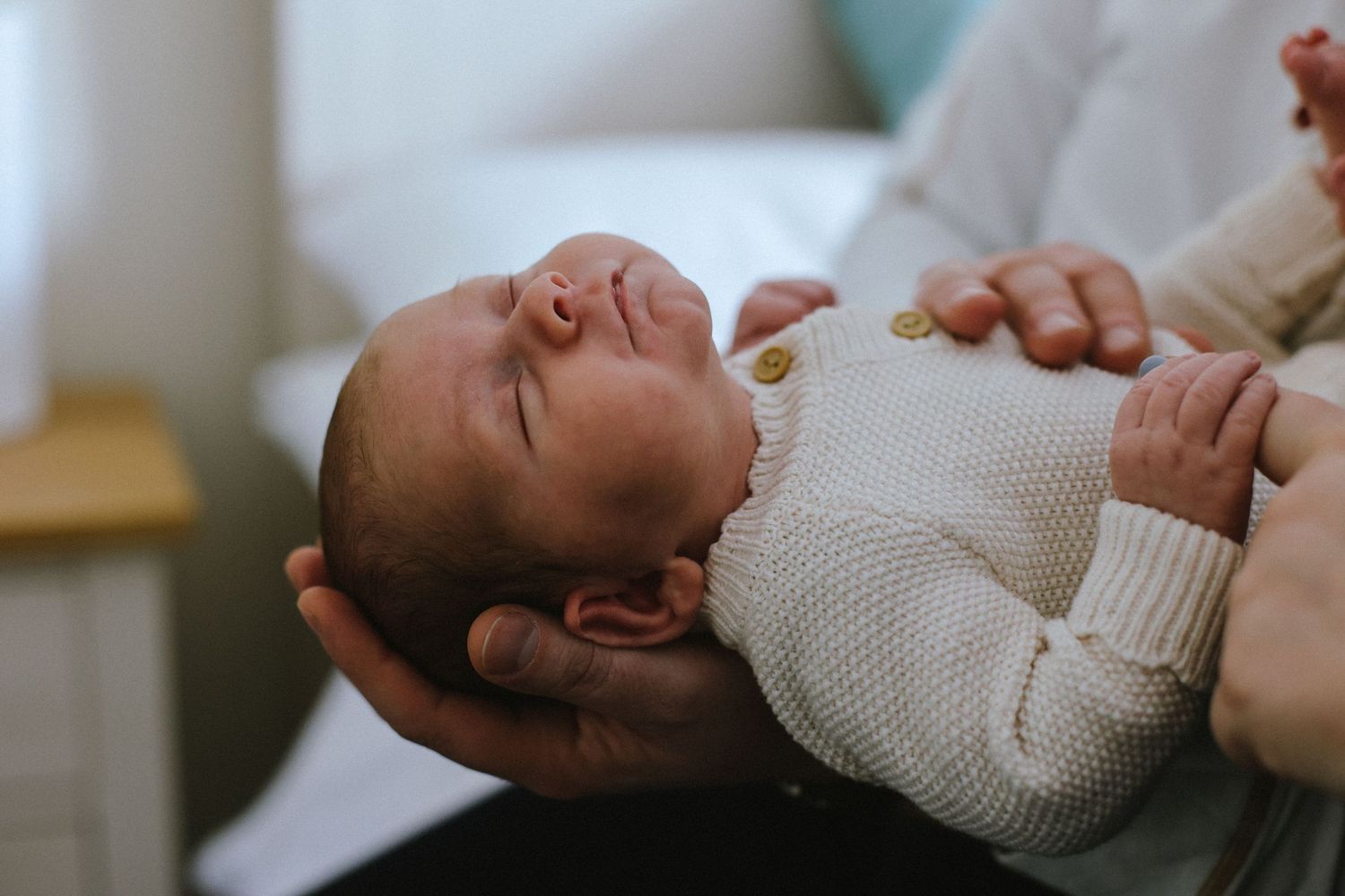Newborn baby in white sweater sleeping peacefully during photo session.