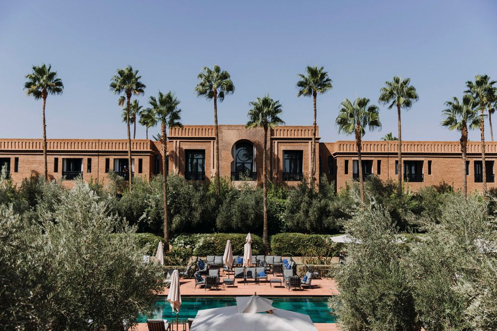 View of Mediterranean style resort with terracotta buildings, palm trees and pool surrounded by olive trees.
