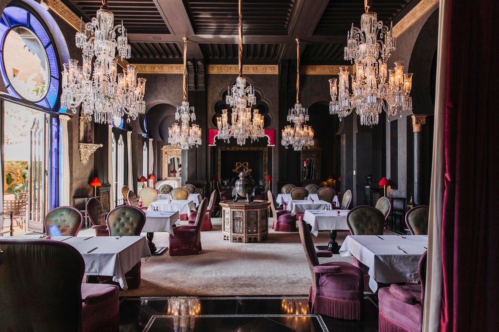 Elegant restaurant interior with crystal chandeliers, white tablecloths, and luxurious purple seating in a classic setting.
