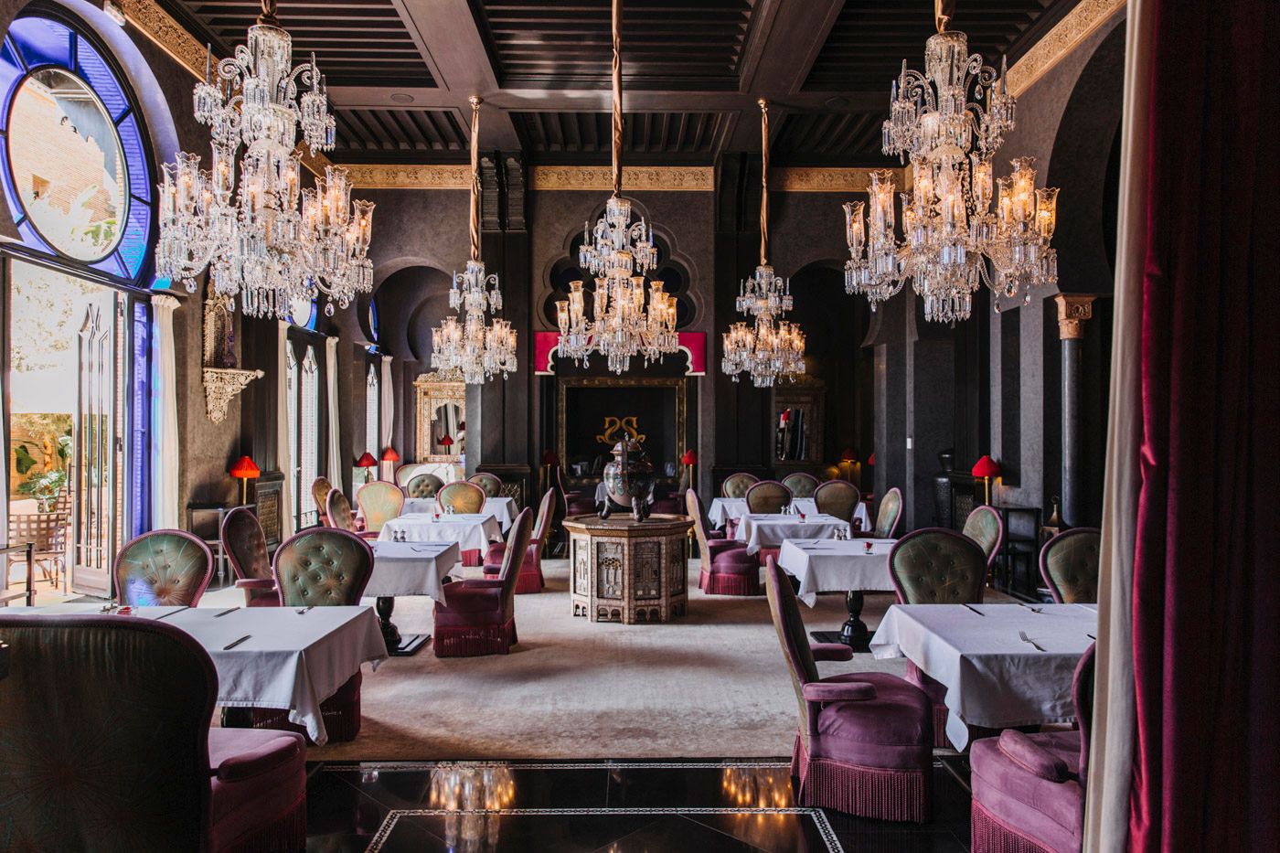 Elegant restaurant interior with crystal chandeliers, white tablecloths, and luxurious purple seating in a classic setting.