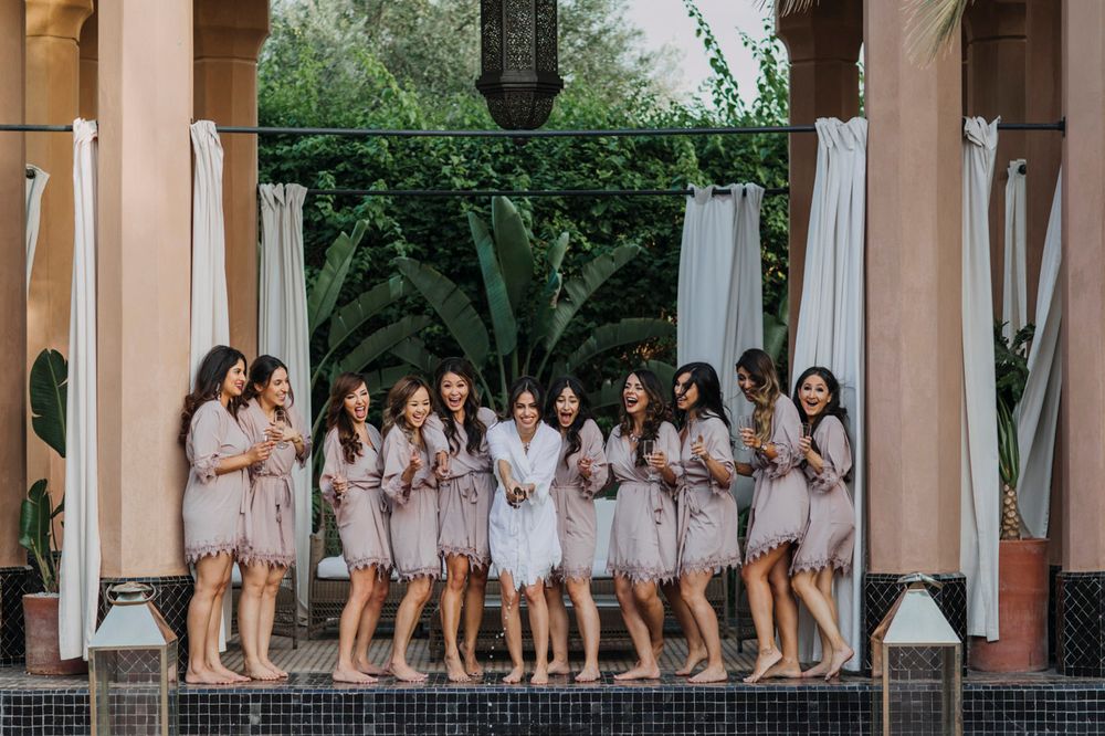 A group in matching light colored robes poses together under an arched patio with white curtains and greenery.