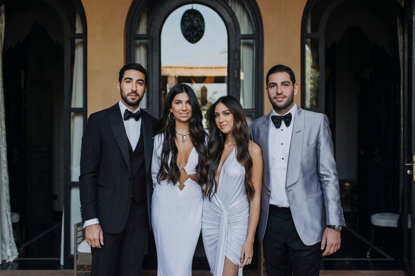 Four elegantly dressed people in formal attire stand together under an arched doorway.
