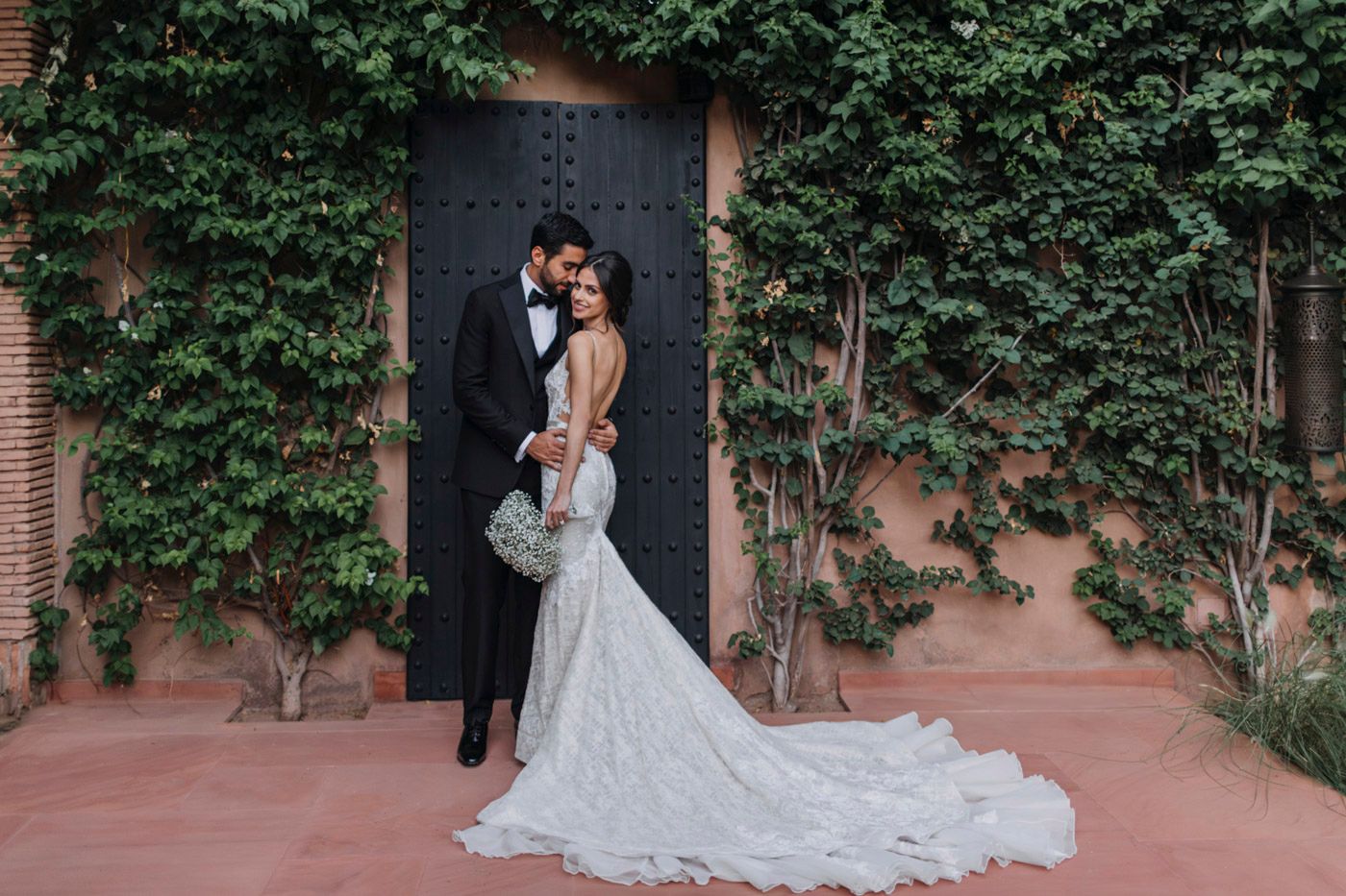 An elegant wedding couple embraces in front of a rustic door surrounded by climbing ivy.