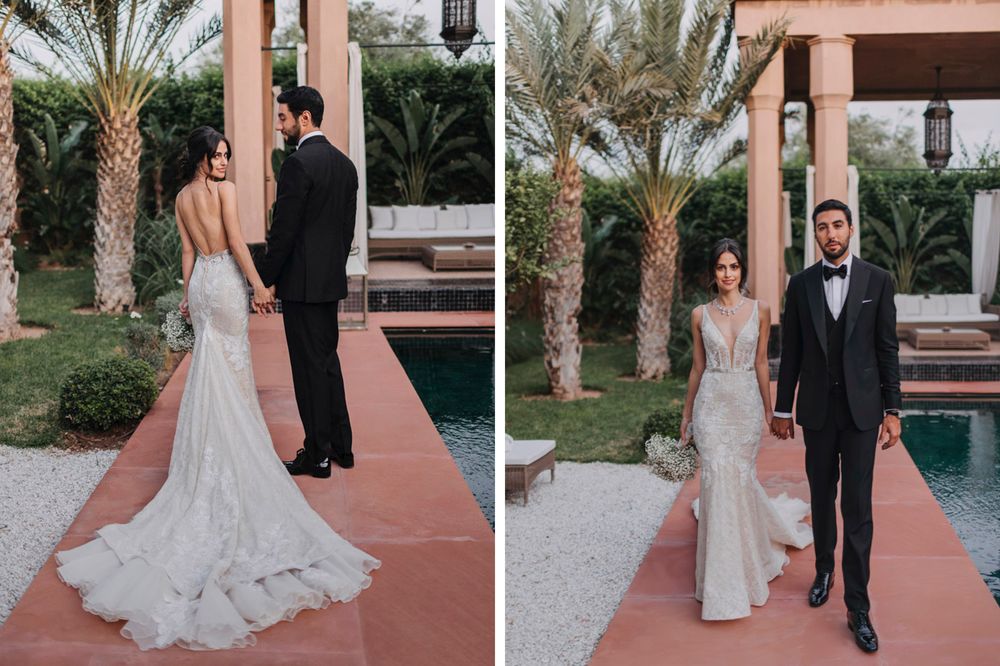 Elegant bride in backless lace gown and groom in tuxedo pose by palm trees and swimming pool.