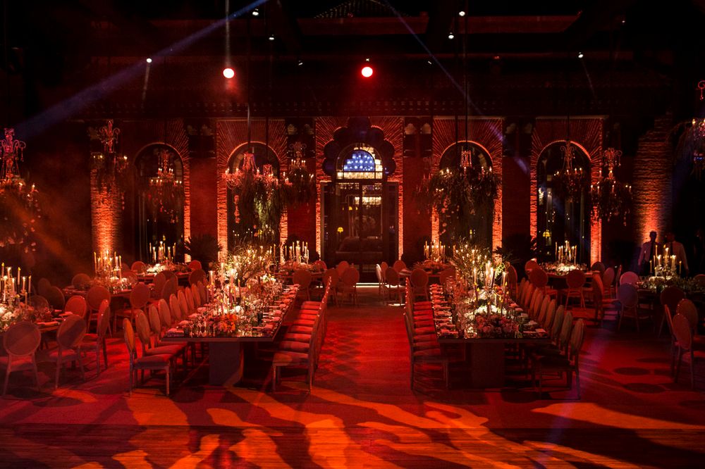 Elegant banquet hall with dramatic red lighting, arched columns, and long dining tables arranged for a formal evening event.
