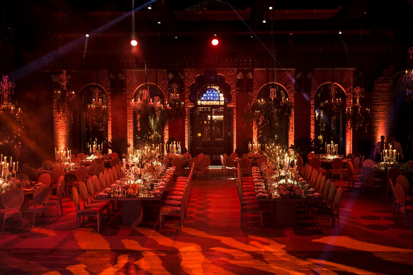 Elegant banquet hall with dramatic red lighting, arched columns, and long dining tables arranged for a formal evening event.