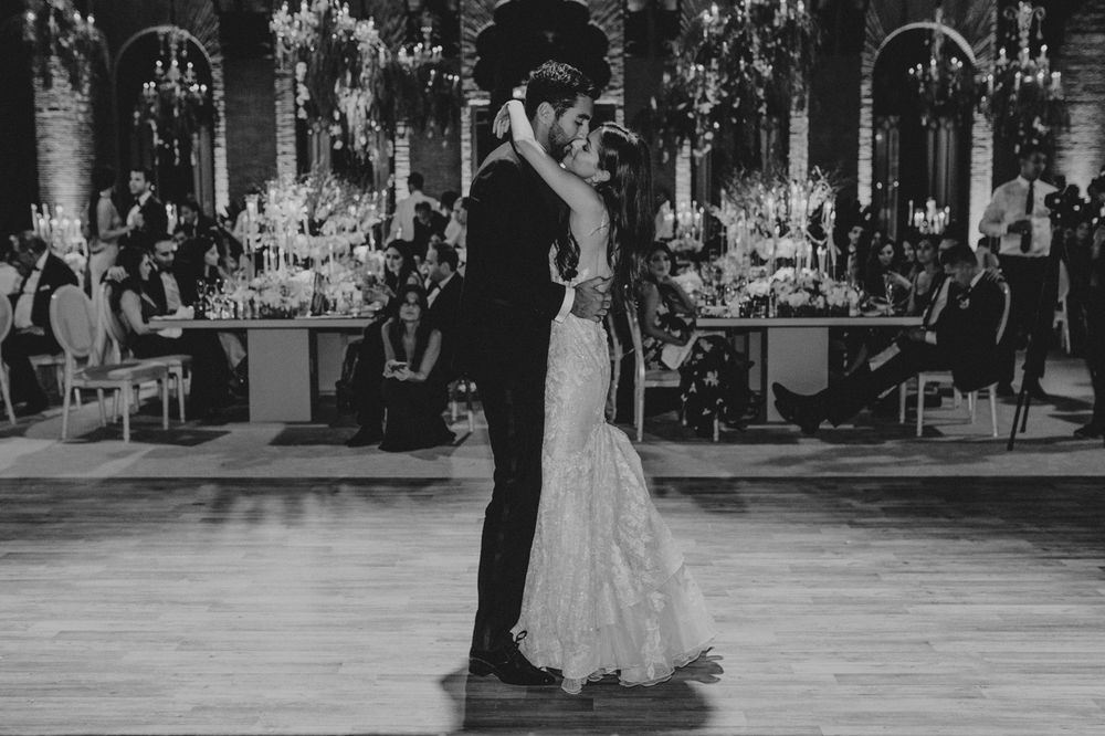 A couple shares their first dance together in a grand ballroom with decorative floral arrangements in black and white.