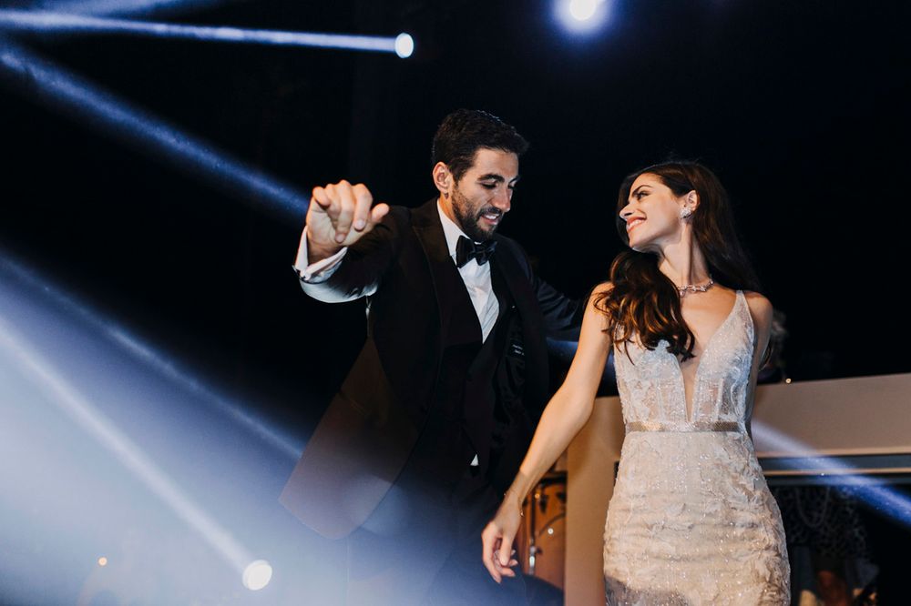 Couple dancing under dramatic spotlight at elegant wedding reception with theatrical lighting effects.
