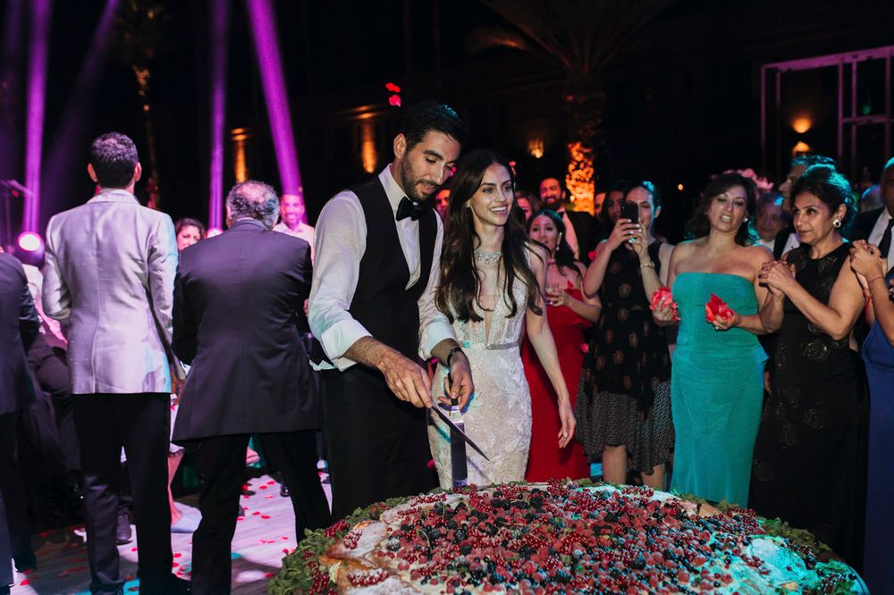 Wedding guests gather around a large decorated cake on the dance floor during an evening reception celebration.