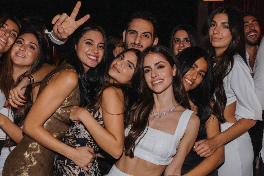 A lively group of friends laughing and posing together at a party in casual and dressy attire.