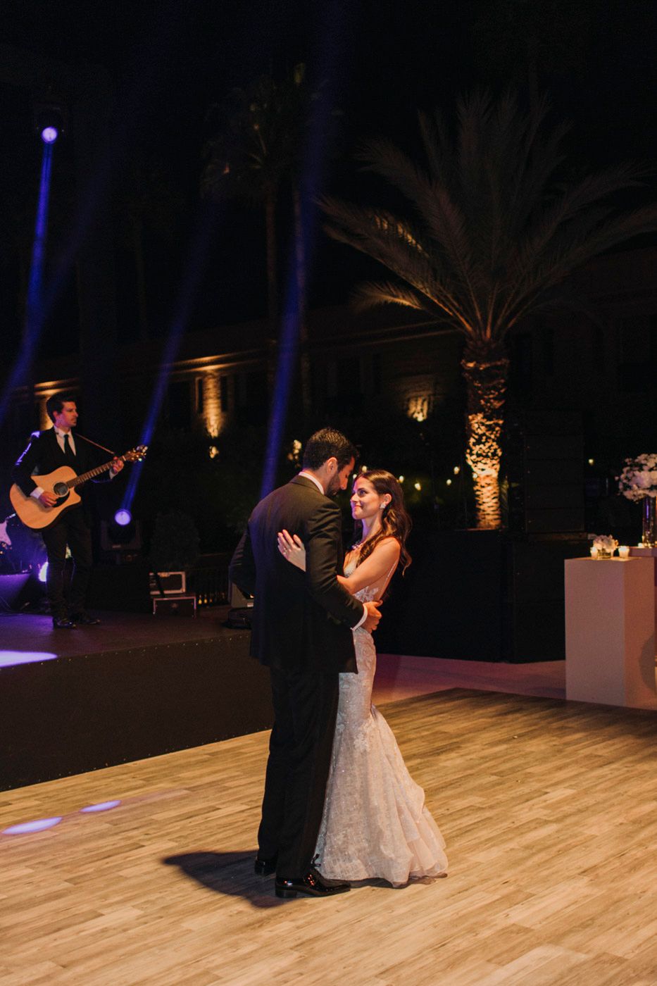 Couple shares romantic first dance at wedding reception with live guitarist and dramatic blue lighting on stage.