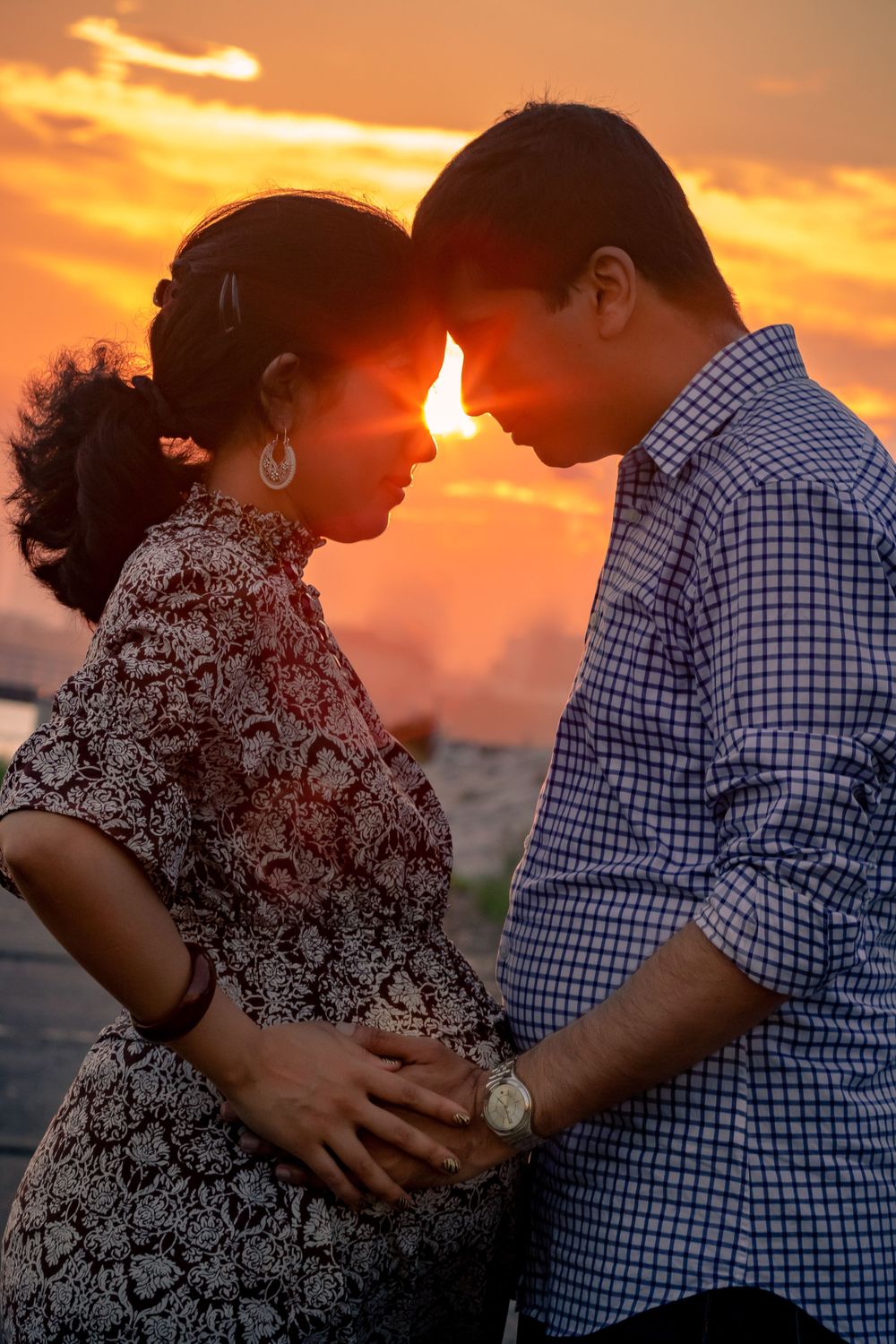 Couple shares an intimate moment against a vibrant orange sunset sky.