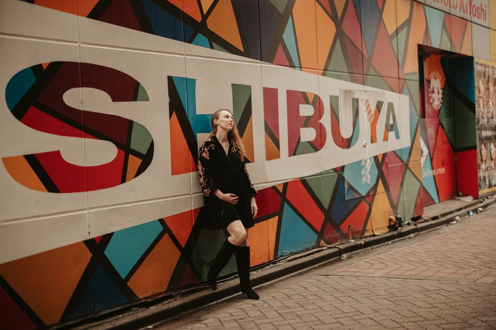 A stylish figure in black poses against a colorful geometric wall with Shibuya text in Tokyo, Japan.