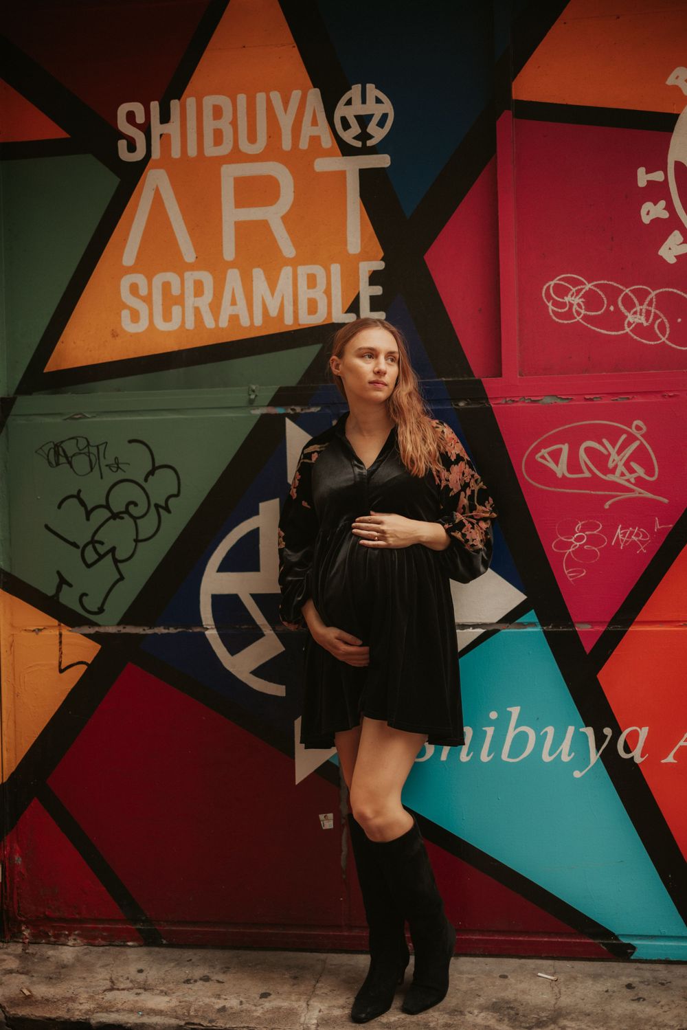A stylish maternity photo against a colorful geometric wall with "Shibuya Art Scramble" text in urban setting.