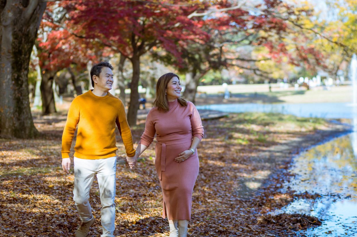 Couple walking along autumn path beside water with colorful fall foliage.