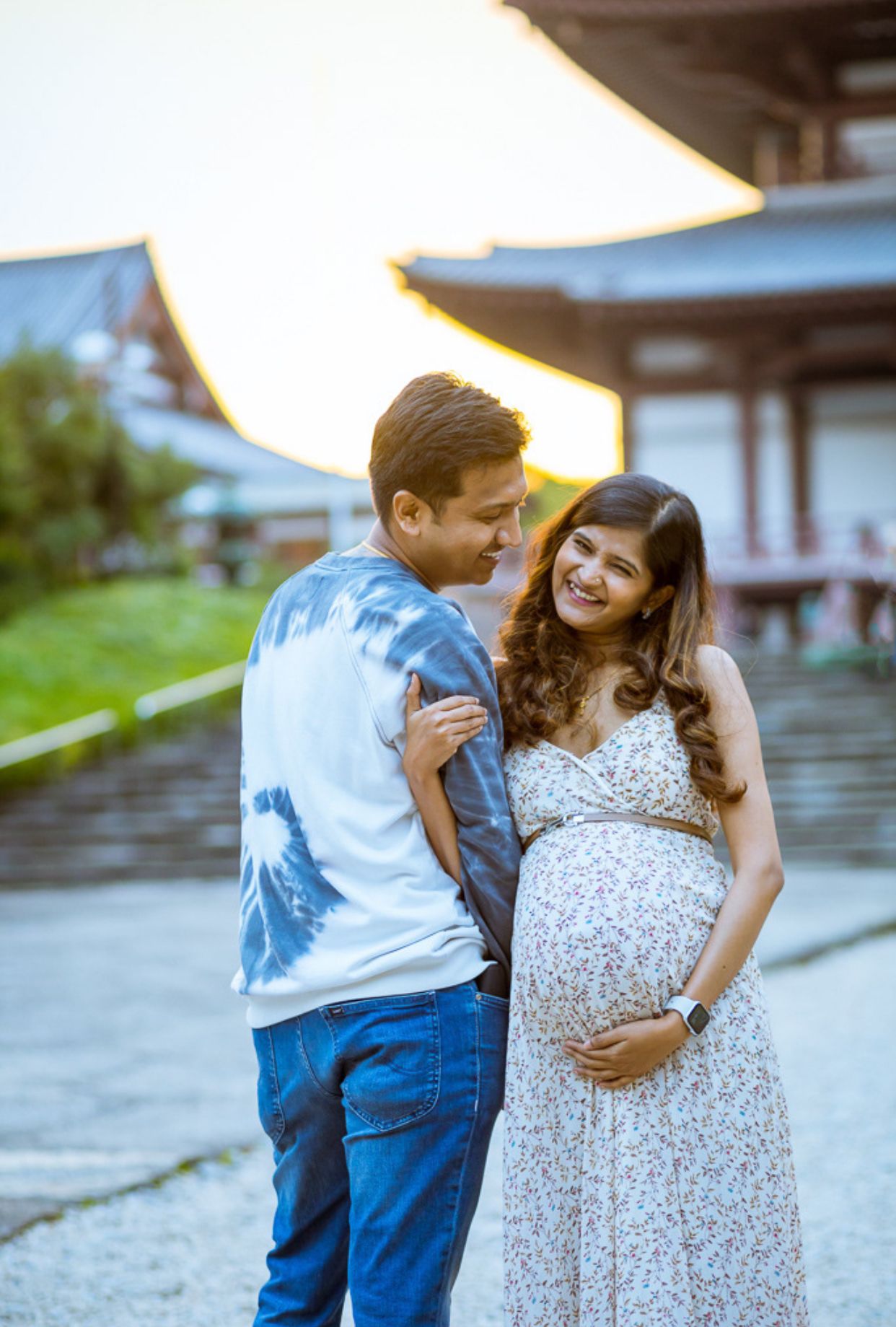 Maternity photo showing couple sharing intimate moment outdoors in casual summer attire.