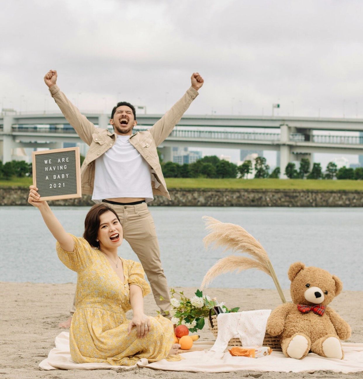 Couple celebrating with teddy bear and picnic by Rainbow Bridge in Tokyo.