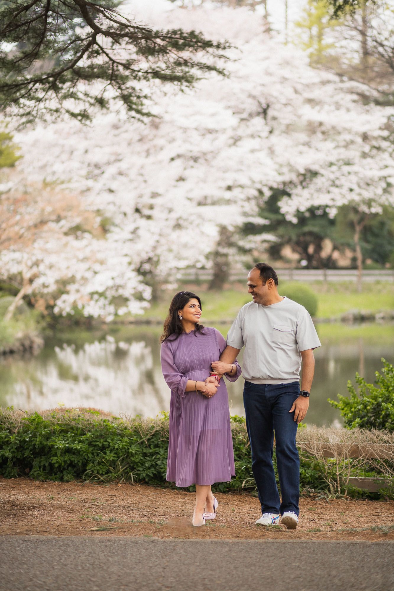 Couple walking together on path by lake surrounded by blooming cherry blossom trees.