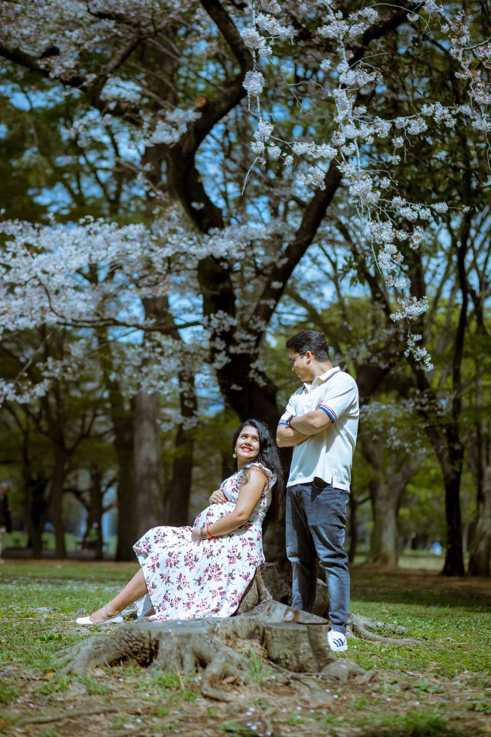 Couple poses under cherry blossom trees in spring park setting.