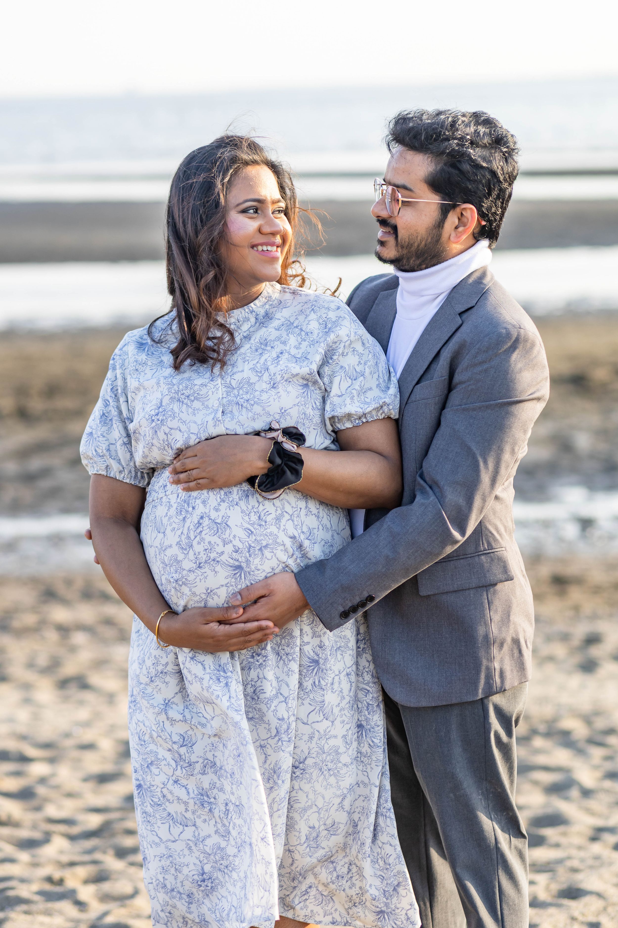 Expecting couple embracing on beach at golden hour.