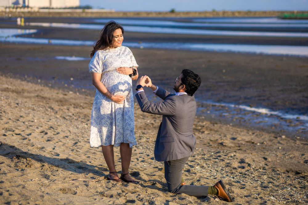 A romantic proposal moment takes place on a sandy beach during sunset with calm water in the background.