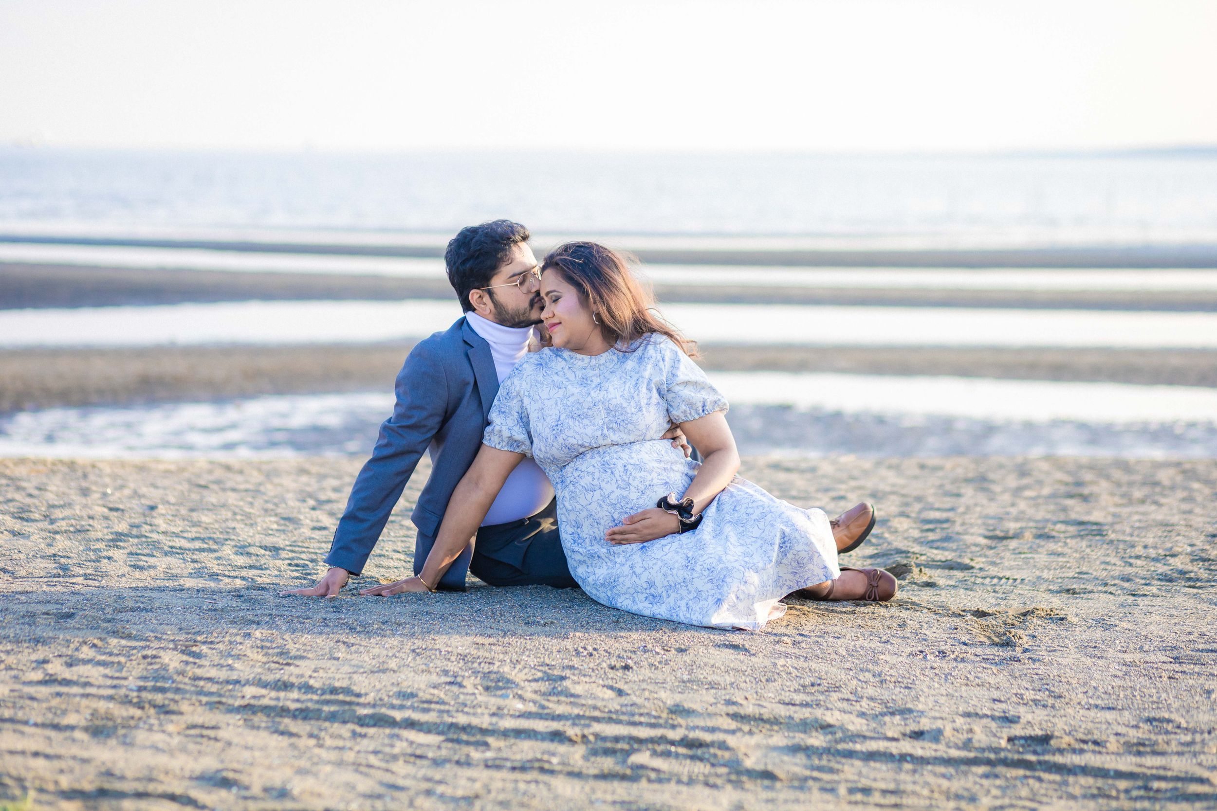 A couple shares an intimate moment while sitting on the beach at sunset.