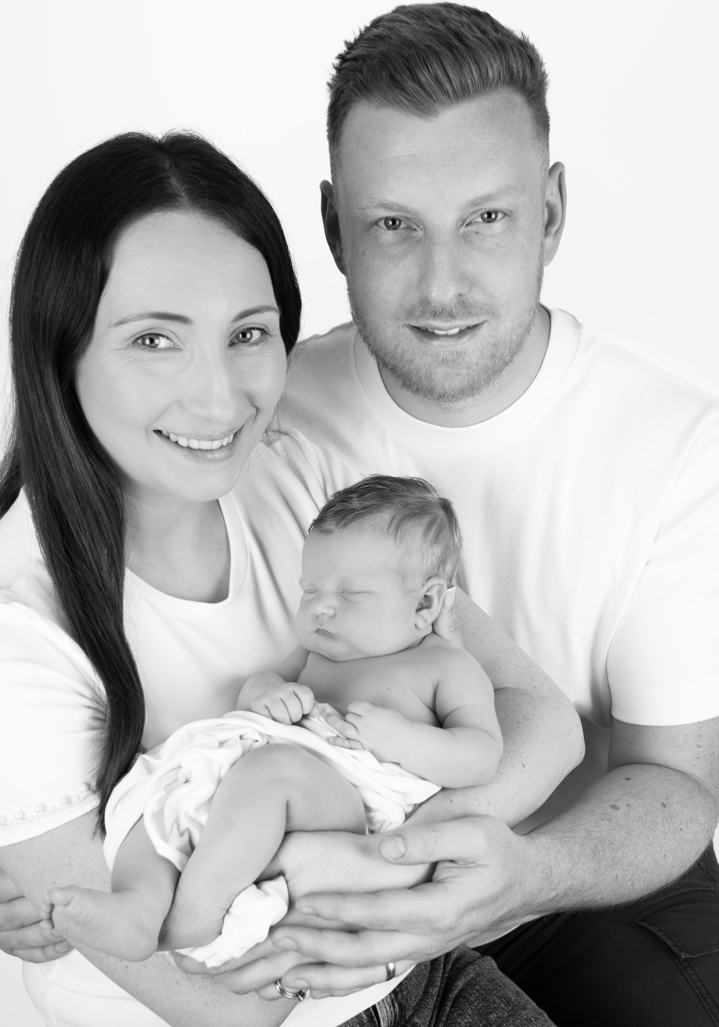 Black and white studio portrait of family with newborn baby.
