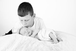 Black and white image of siblings sharing tender moment on white blanket.