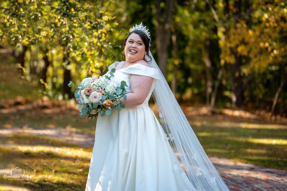 Bride in white wedding dress poses outdoors in autumn setting with golden foliage.