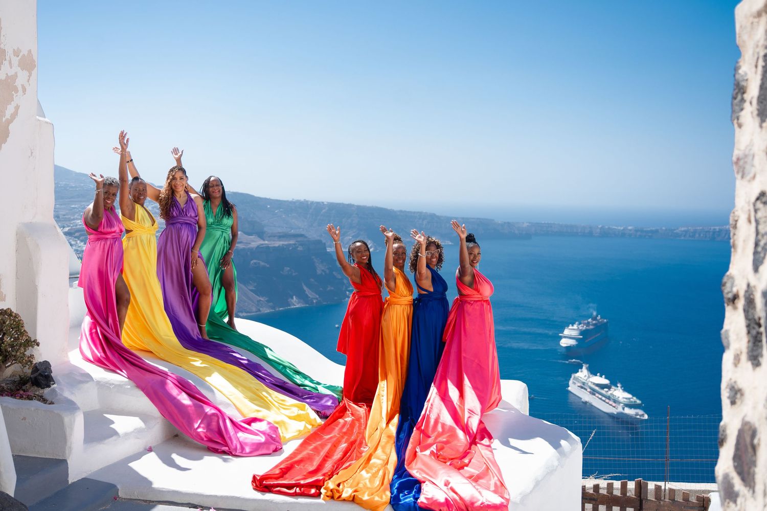Group in colorful flowing dresses posing on white rooftops overlooking Mediterranean Sea.