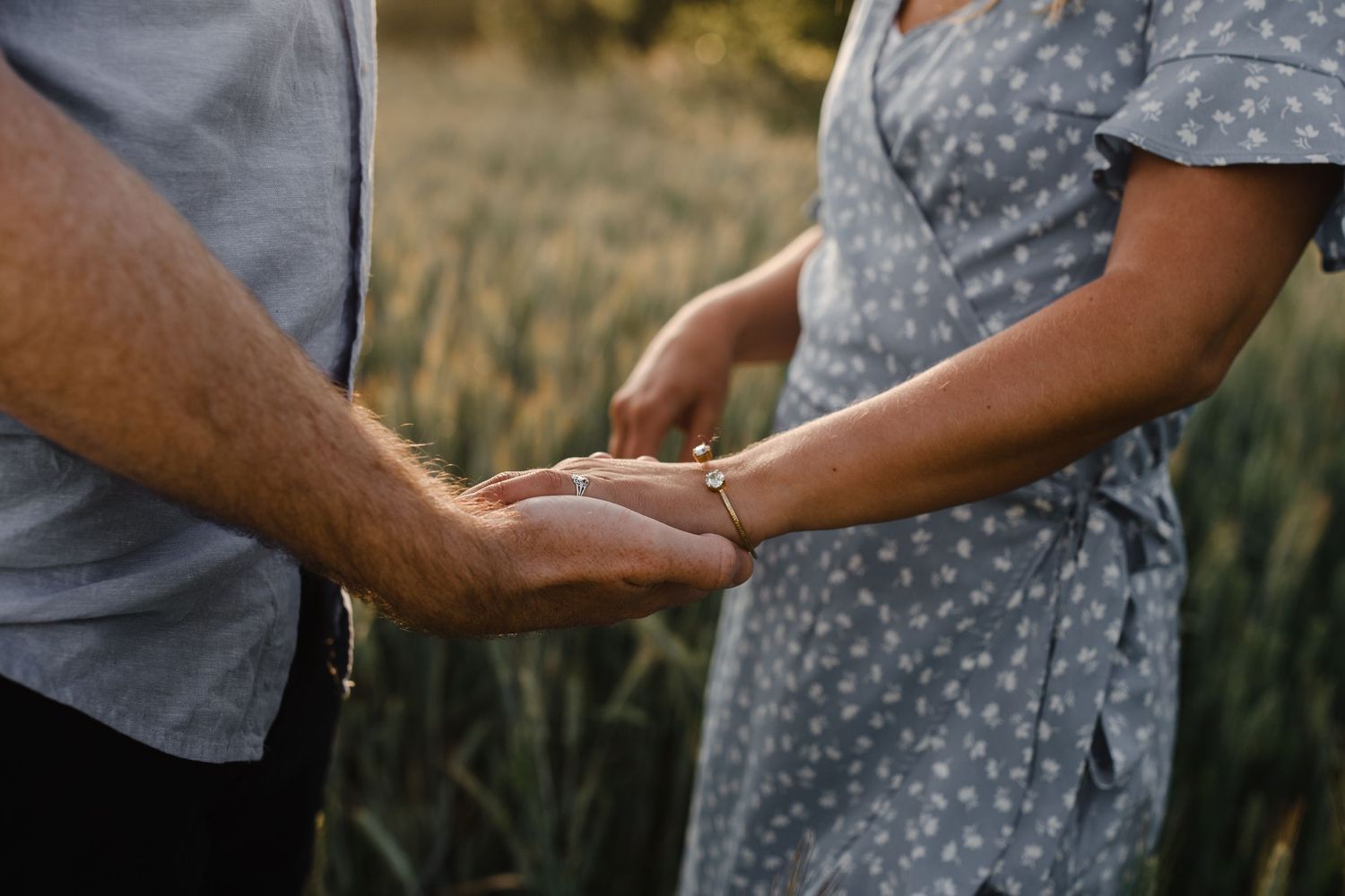 Close-up of two people holding hands in a field during golden hour.