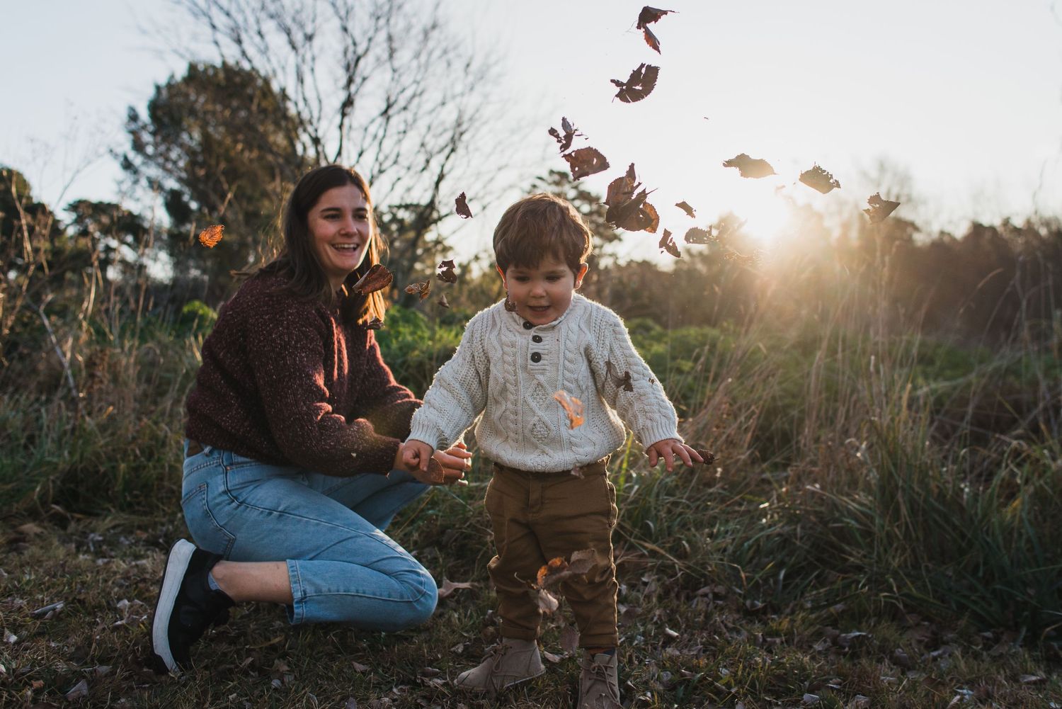 madre arrodillada jugando con su hijo de un año con hojas de otoño