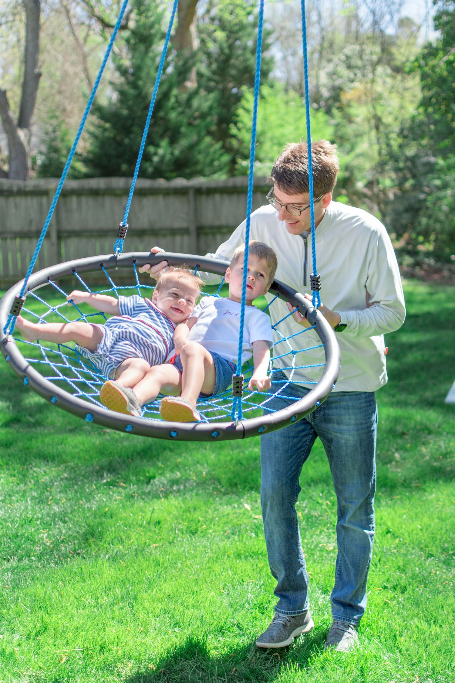 Dad pushes his two boys on their disk swing in the back yard.