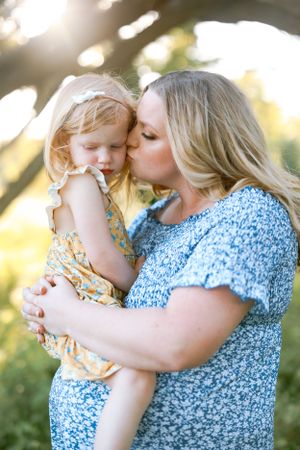 A tender moment captured in sunlight shows a parent embracing and kissing a small child in a floral print outfit.