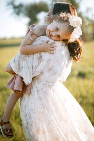 A tender embrace between figures in a sunny field, wearing white flowing dresses and delicate floral accessories.