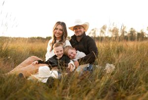 Family sitting together in a golden autumn field with tall grass at sunset for outdoor portrait session.