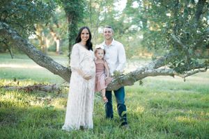 Family poses together outdoors under a tree branch in a sunlit grassy field during golden hour.