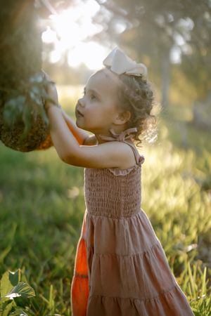 A candid shot in sunset lighting shows a young child in a brown tiered summer dress playing outdoors.