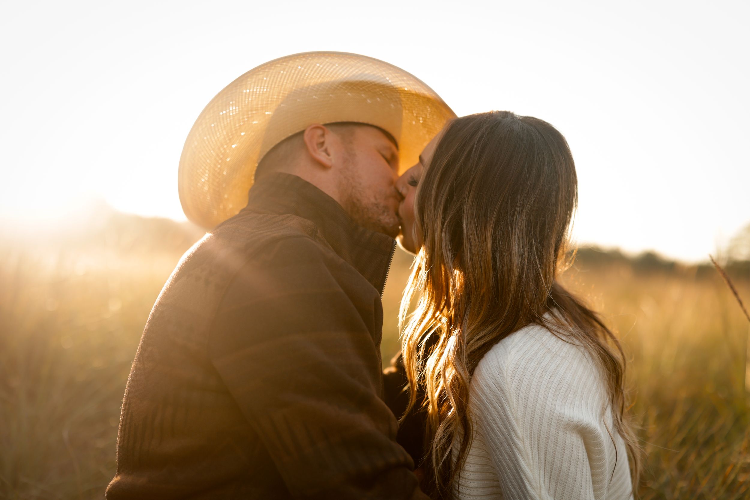 portrait of cinematic couple in field at golden hour kissing and sharing romantic emotive moment