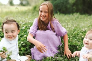 A joyful moment captured in a field of greenery on a sunny summer day, with people wearing light purple and white.