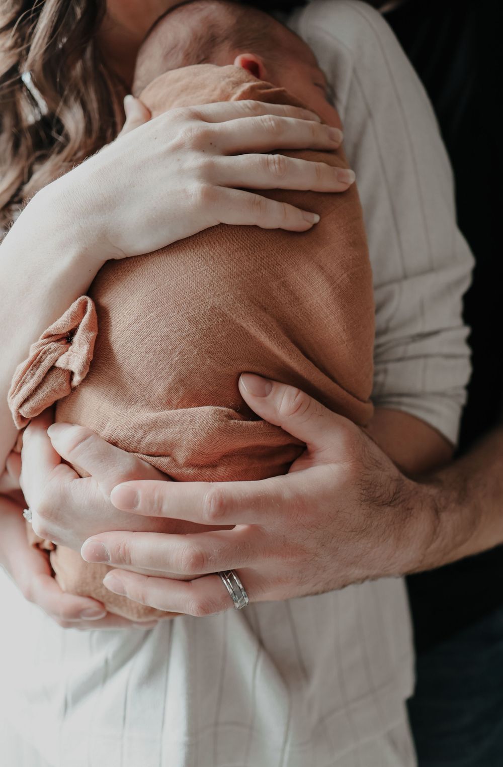 Close-up of hands tenderly holding sleeping newborn wrapped in soft fabric.