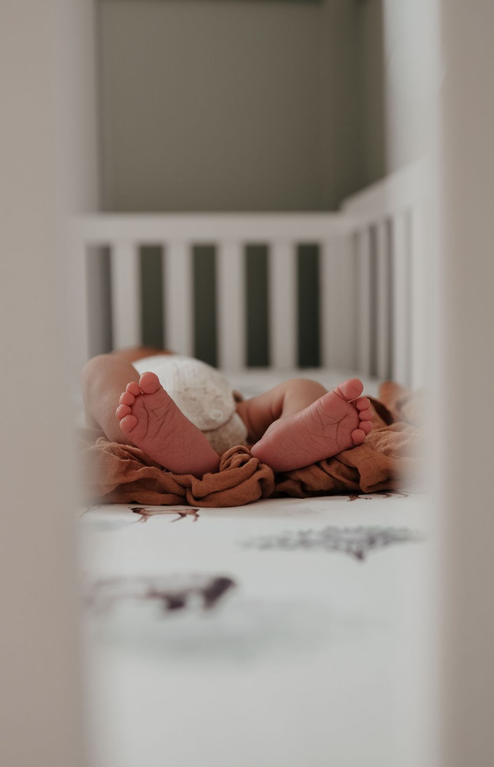 Baby's tiny feet peeking through crib slats against neutral bedding.