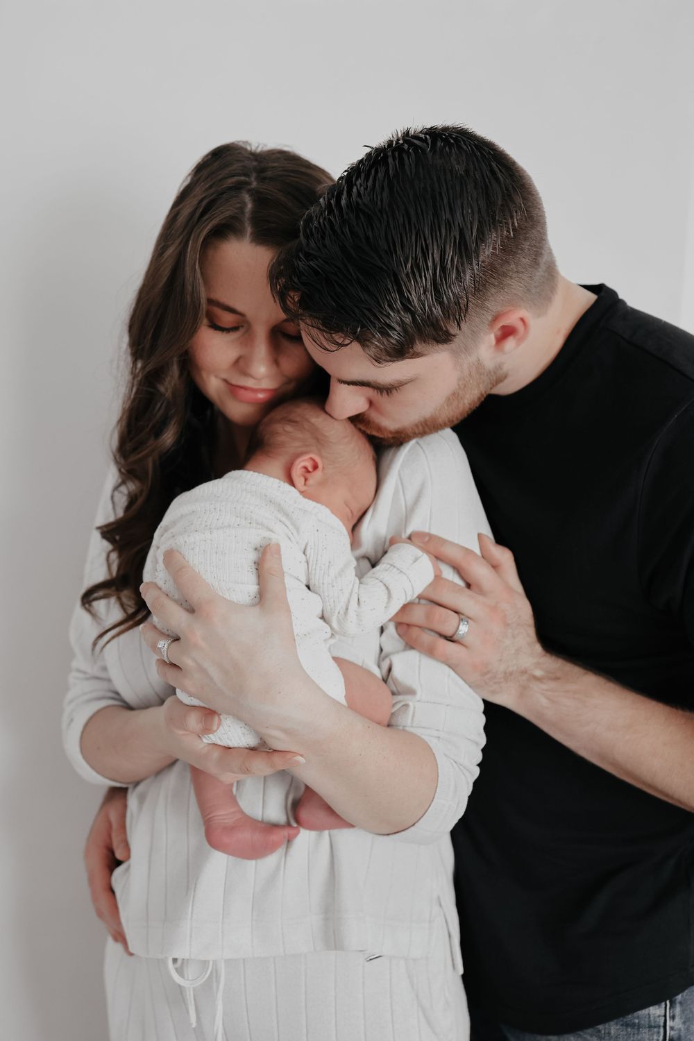 Parents sharing intimate moment kissing their newborn baby against white background.
