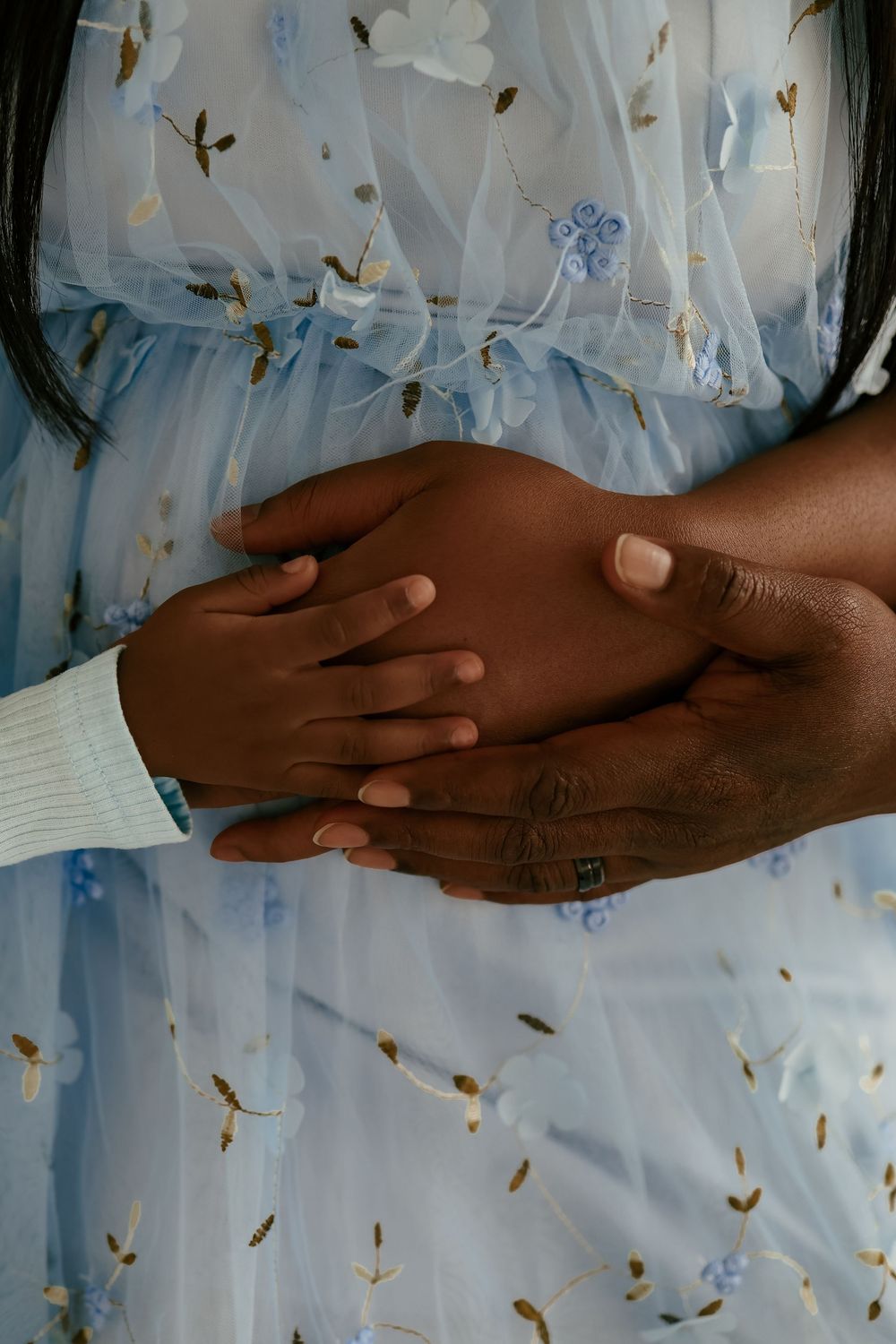 Two hands with different skin tones join together in a comforting gesture against a light patterned background.